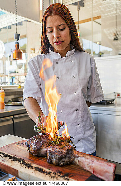 Female chef smoking steak in kitchen