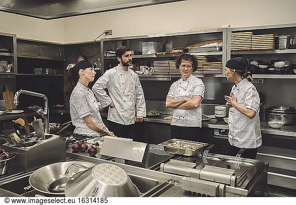 Female chef talking to coworkers in commercial kitchen