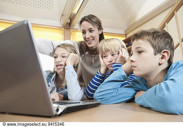 Female childcare assistant and three boring children looking at laptop