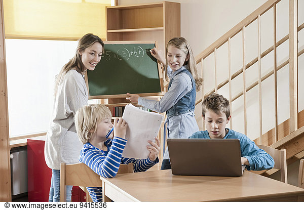 Female childcare assistant helping children by doing homework