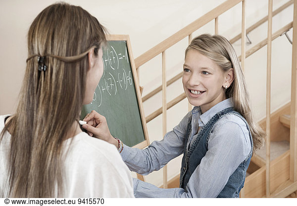 Female childcare assistant helping schoolgirl by doing homework
