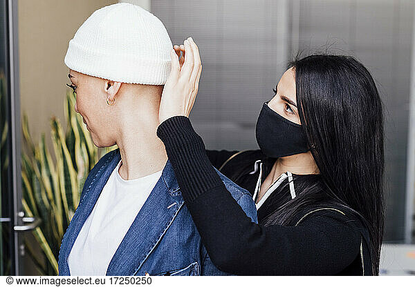 Female colleague in face mask helping businesswoman wearing knit hat at office