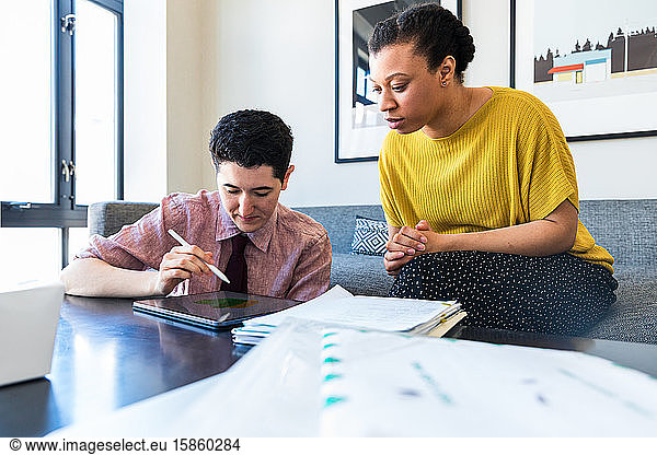 Female colleague looking at businessman using graphics tablet while sitting in office