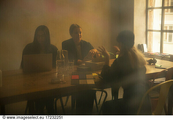 Female colleagues discussing in board room seen through through glass of office