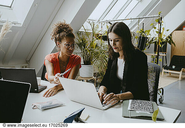 Female colleagues discussing over laptop at coworking office