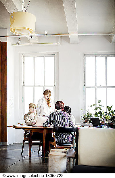 Female colleagues having discussion at conference table in creative office