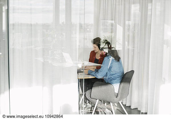 Female colleagues working in office seen through glass