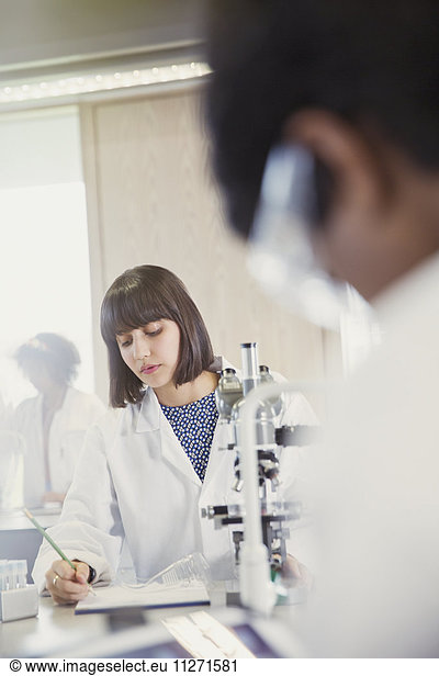 Female college student conducting scientific experiment at microscope in science laboratory classroom