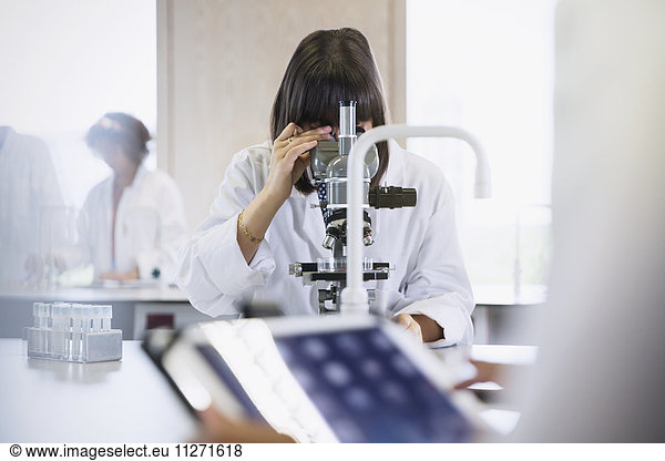Female college student using microscope in science laboratory classroom