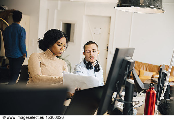 Female computer hacker showing document to male coworker while sitting in office