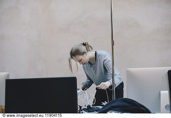 Female computer programmer fixing tangled cables against wall in office