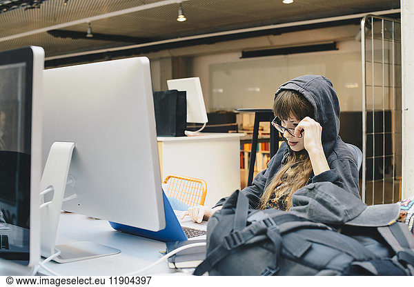 Female computer programmer using laptop while looking over eyeglasses in office
