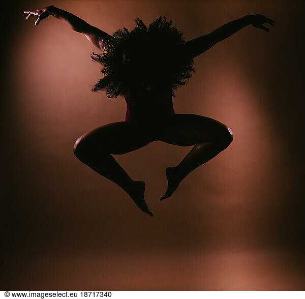 Female curly hair dancer in jump dance pose silhouette in studio