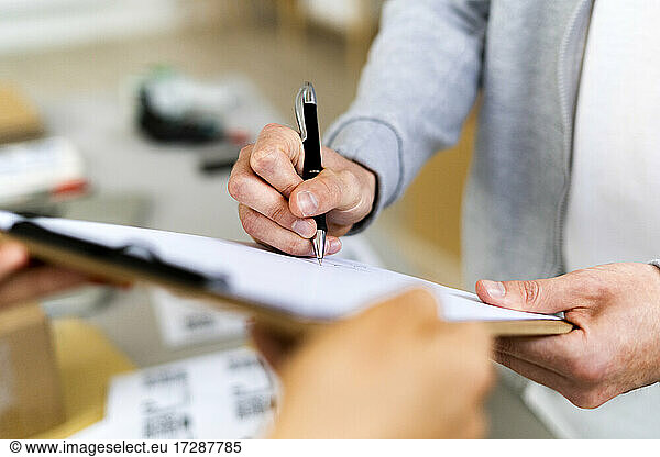 Female customer signing on document after receiving package in warehouse