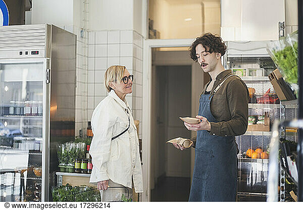 Female customer talking with male entrepreneur while buying food from store