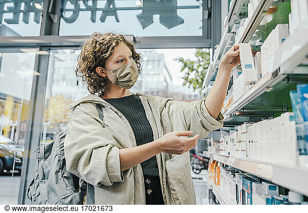 Female customer wearing protective face mask while checking medicine in chemist shop