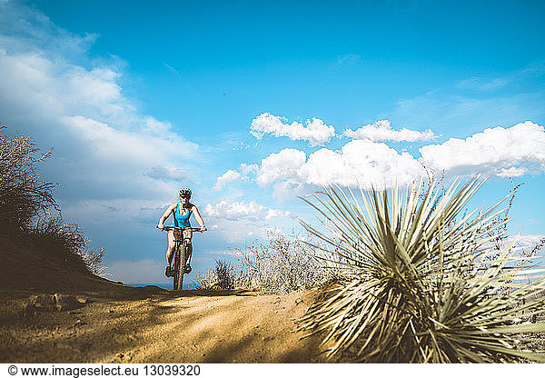 Female cyclist riding mountain bike on dirt trail against blue sky