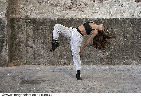 Female dancer dancing while hair tossed against wall in abandoned factory