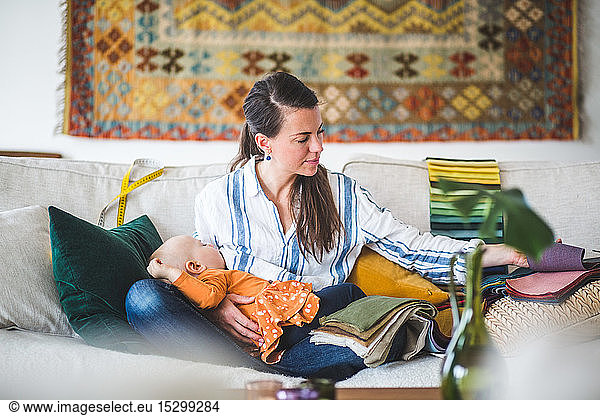 Female design professional with sleeping daughter looking at fabric swatch at home office