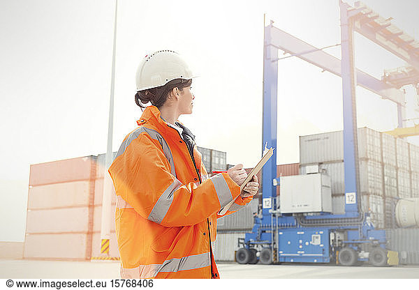Female dock manager with clipboard watching cargo containers