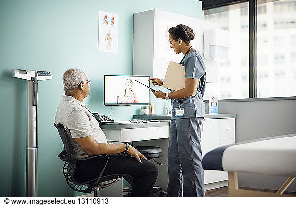 Female doctor discussing with colleague on conference call while patient sitting in clinic