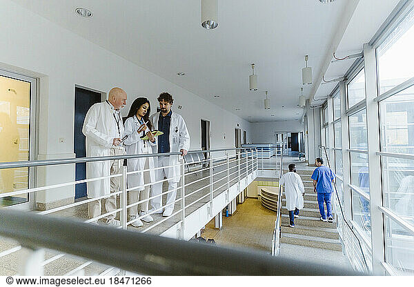 Female doctor discussing with colleagues in corridor at hospital