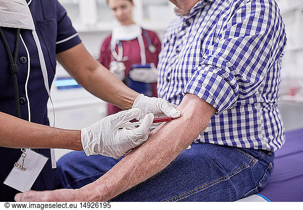 Female doctor drawing blood from senior male patient in clinic examination room