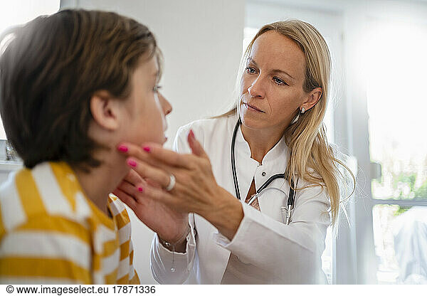 Female doctor examining boy touching his neck