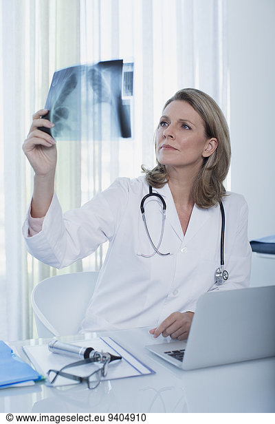 Female doctor looking at x-ray at desk with laptop in office