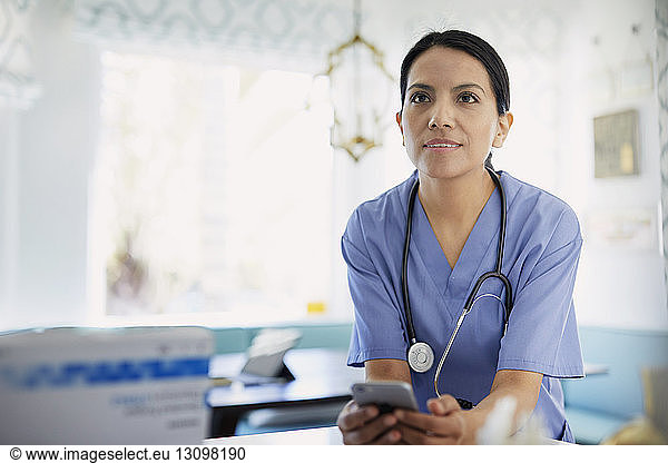 Female doctor looking away while holding smart phone in hospital