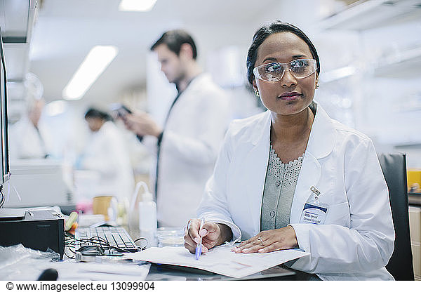 Female doctor looking away while working at desk with coworkers in background
