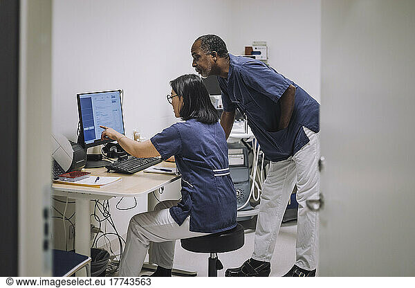 Female doctor pointing at computer monitor while discussing with male colleague in hospital