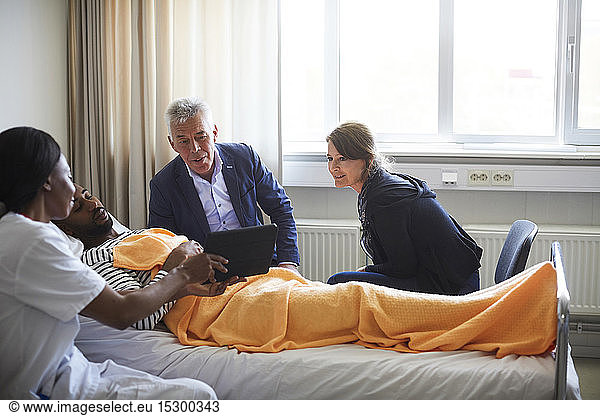Female doctor showing digital tablet to patient with family in hospital ward