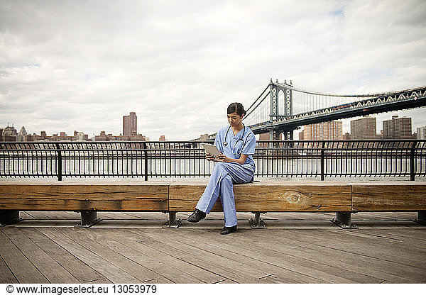 Female doctor sitting on bench against Manhattan bridge in city