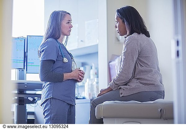 Female doctor talking to patient sitting on bed in medical room