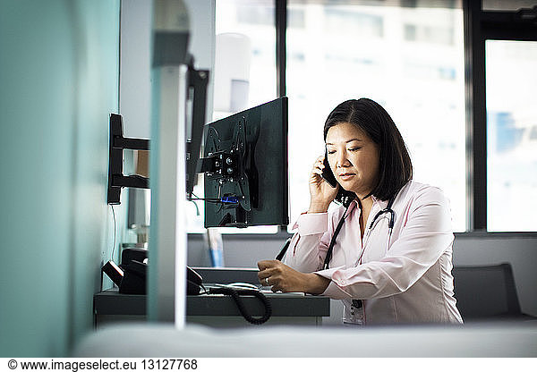 Female doctor using smart phone computer desk in clinic