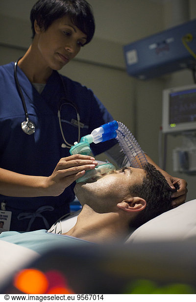 Female doctor wearing mask anesthetizing mid adult man in hospital ward