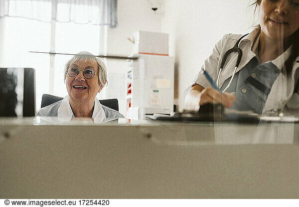 Female doctor writing prescription by senior nurse looking away