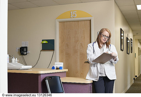 Female doctor writing while standing in corridor