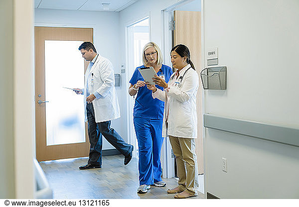 Female doctors discussing over tablet computer while male colleague walking by in hospital