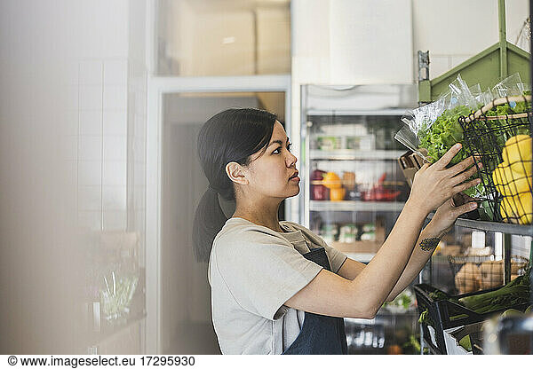 Female employee arranging vegetables on rack in store
