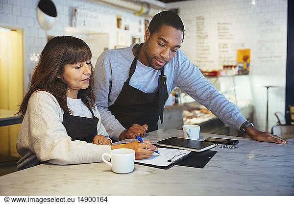 Female employee discussing over clipboard with male coworker at table in cafe