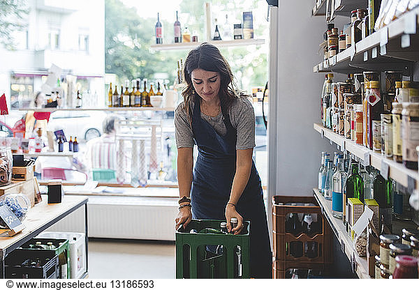 Female employee removing bottle from crate while standing in deli