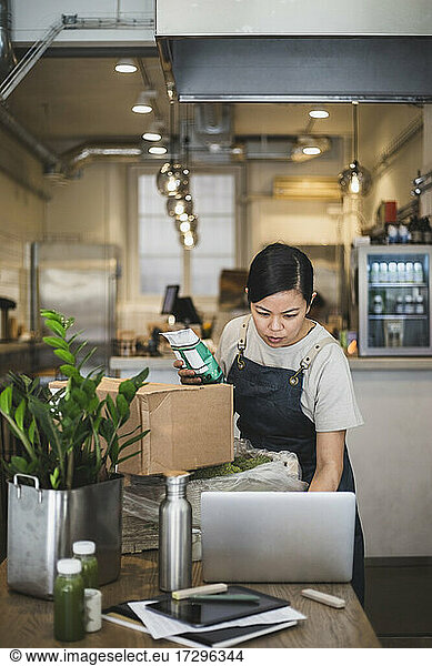 Female employee working laptop while holding food package at store