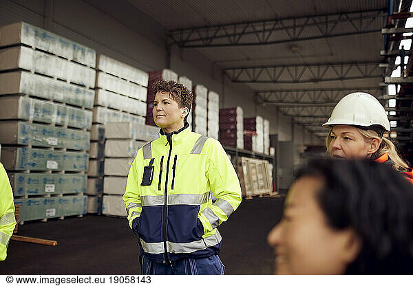 Female engineer in reflective clothing standing with hands in pockets at factory