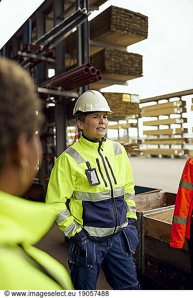 Female engineer with hands in pockets standing at lumber industry