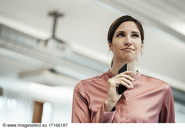 Female entrepreneur contemplating with smart phone in office