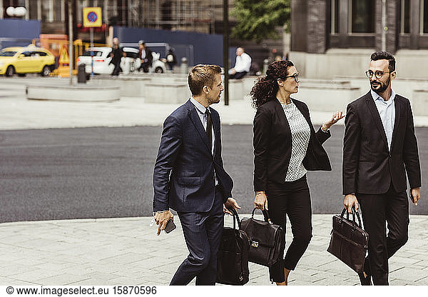 Female entrepreneur discussing business strategy with male coworkers while walking outdoors