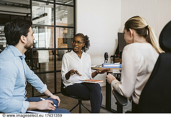 Female entrepreneur discussing plan while sitting with colleagues in office