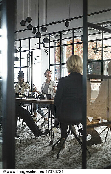 Female entrepreneur discussing with colleagues seen through doorway of startup company